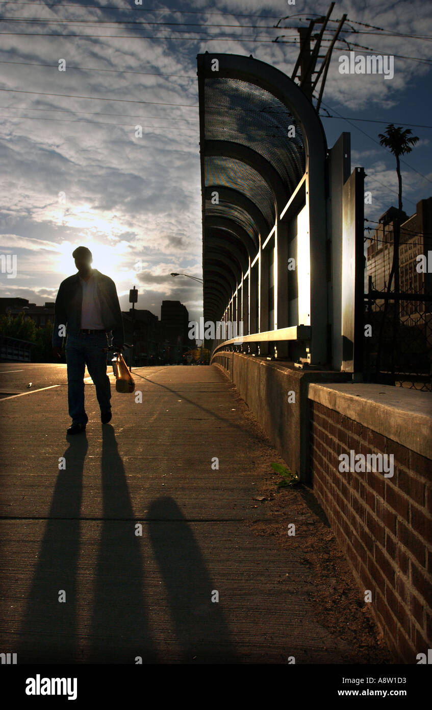Man with shadow walking across bridge on sidewalk dramatic city scene ...