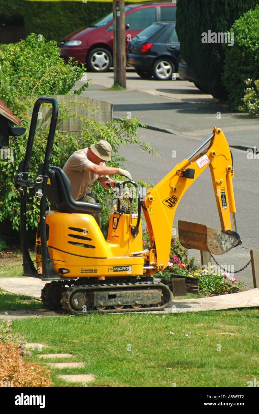 Man controlling Mini excavator crawling across domestic front garden lawn over plywood sheets laid down for protection Essex England UK Stock Photo
