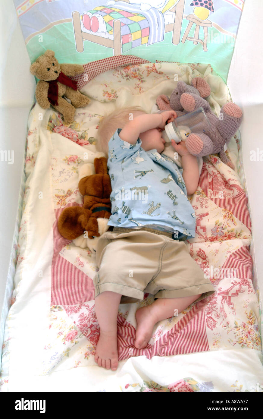 An eightmonth old baby boy sleeping in his cot with his bottle still