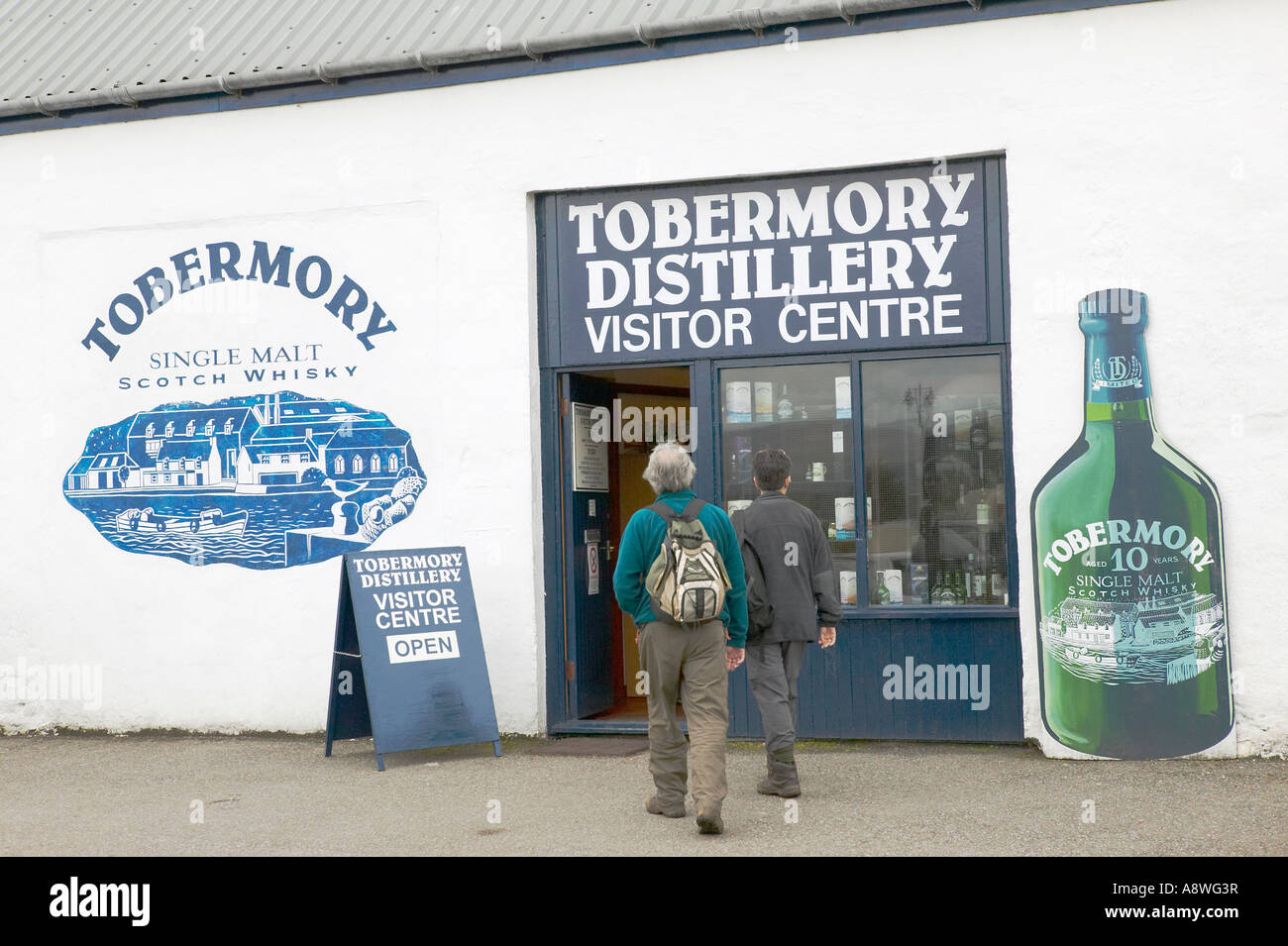 Two tourists walking towards the Tobermory Distillery Visitor Centre at Tobermory Isle of Mull Scotland Stock Photo