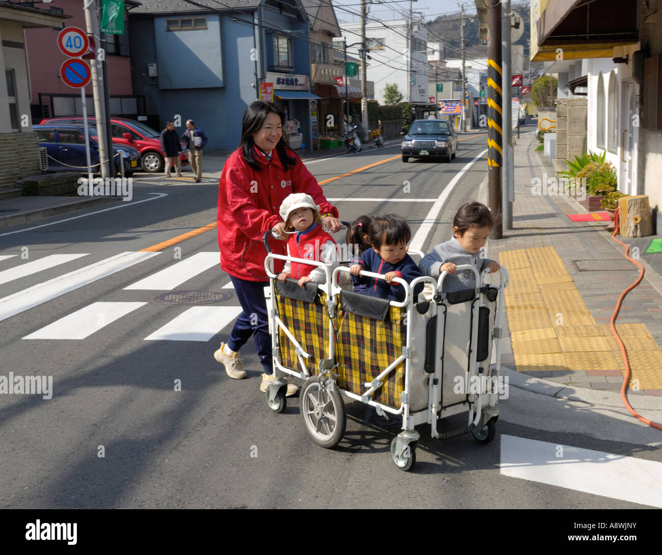 Small children in a trolley are pushed across the street, Kamakura, Japan Stock Photo