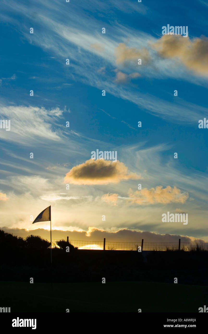 The last hole of the day.The flag on the 18th hole flutters in the wind as the sun sets. Stock Photo