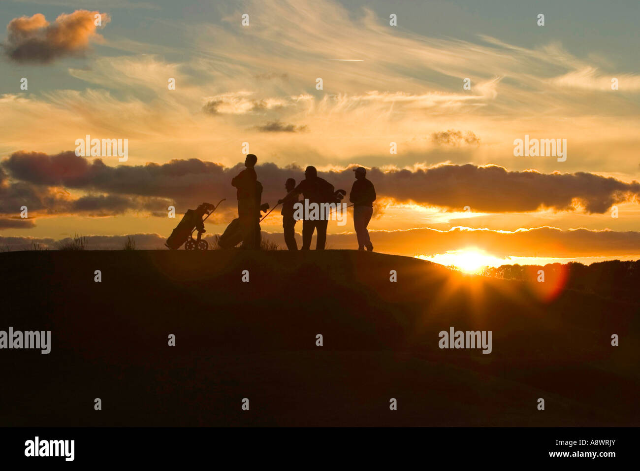 The last hole of the day. Five golfers stand on the last tee as the sun sets. Stock Photo