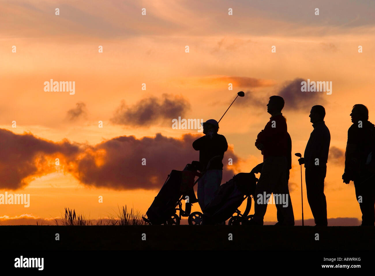 The last hole of the day.Five golfers stand on the last tee in the setting sun. Stock Photo