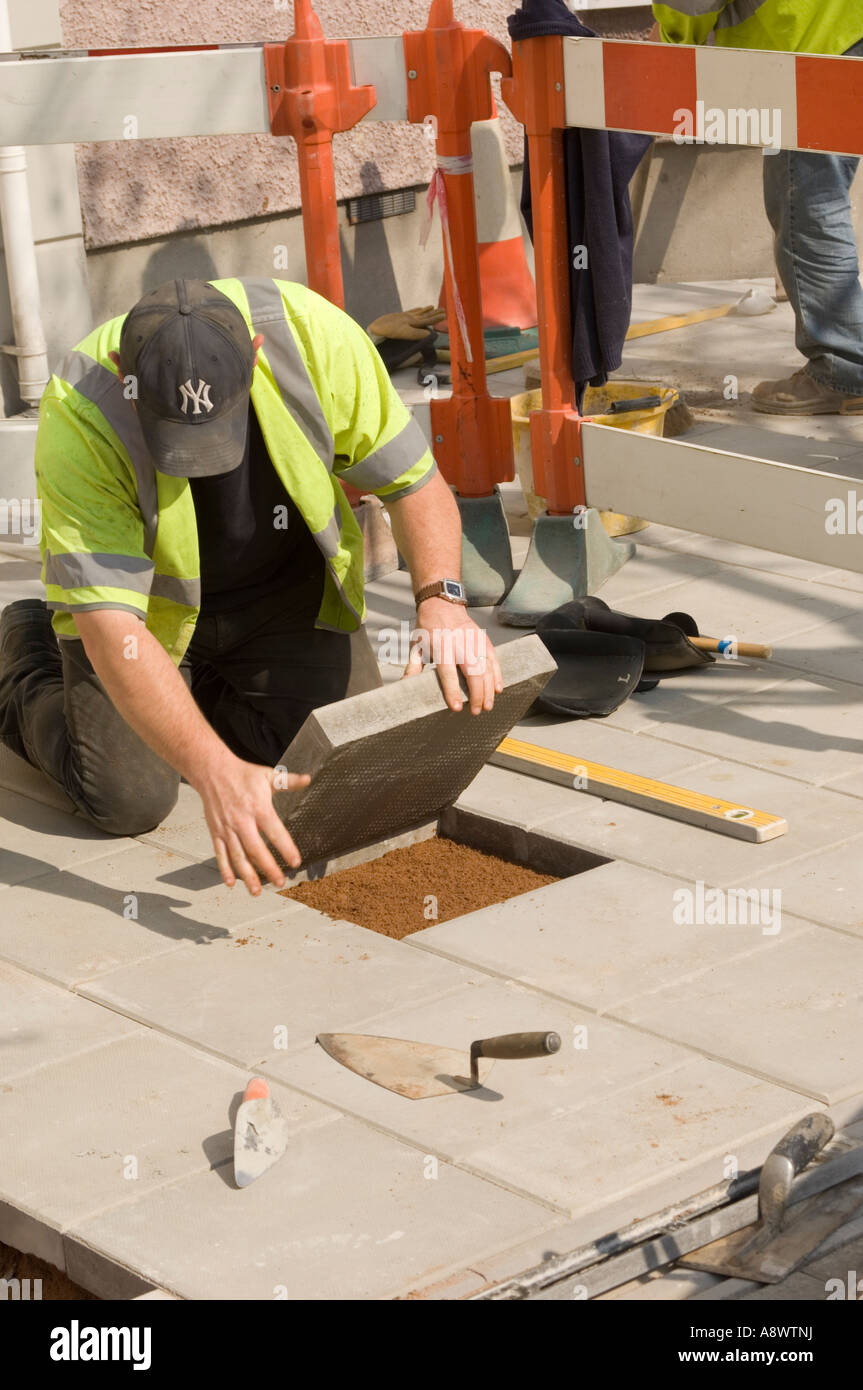 Manual labourer kneeling down and laying concrete pavement side walk slab in the street Stock Photo