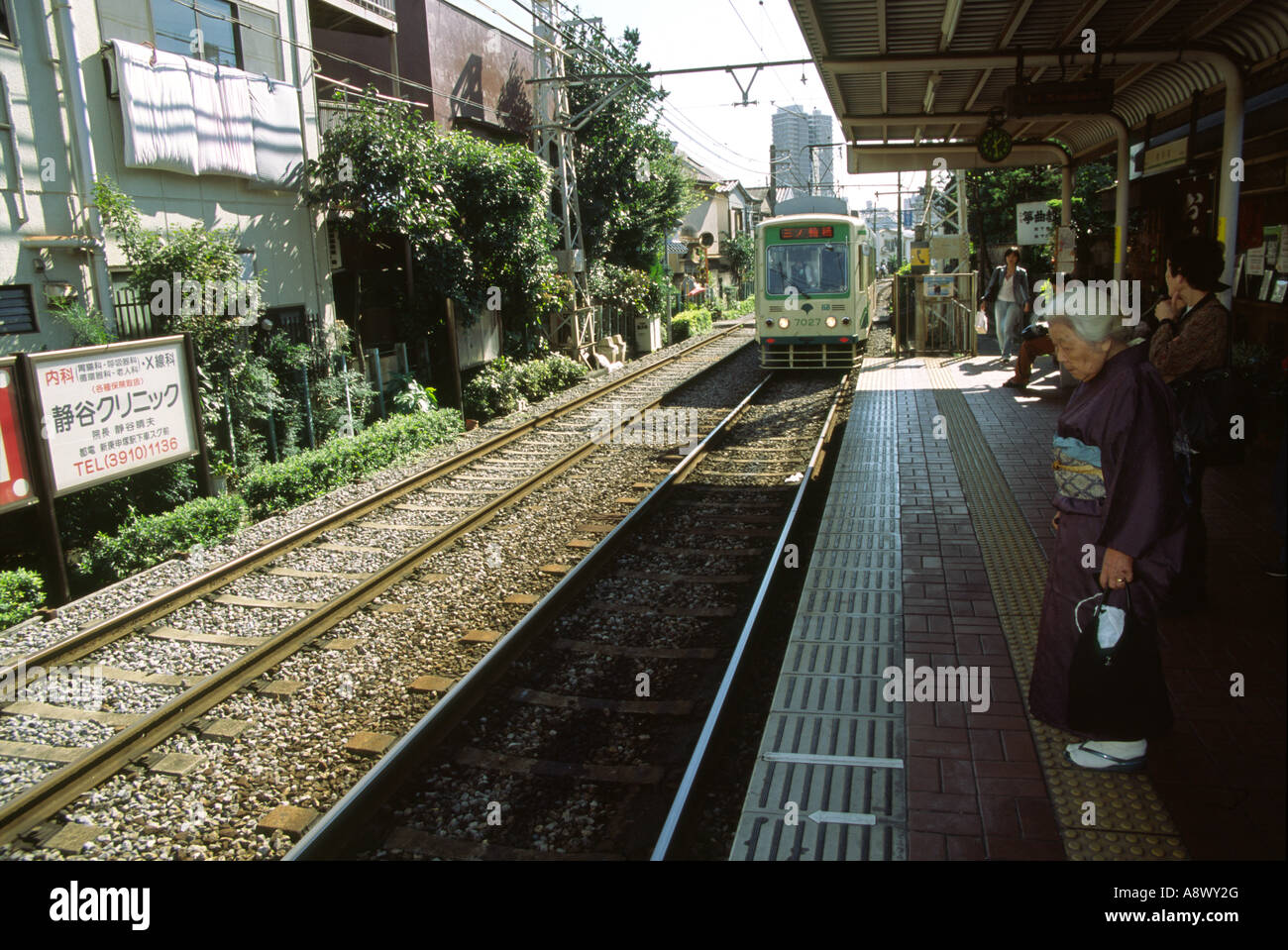 An old lady in a kimono waits at a station for a tram or street car on ...