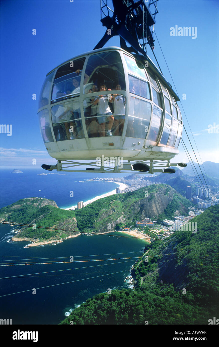 Cable car loaded with passengers nearing top of Sugar Loaf or Pao de Acucar with shorelines of Rio de Janeiro below Stock Photo