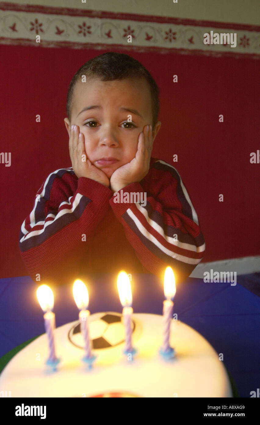 Four year old boy looks unhappy blowing out the candles on his Birthday cake UK Stock Photo