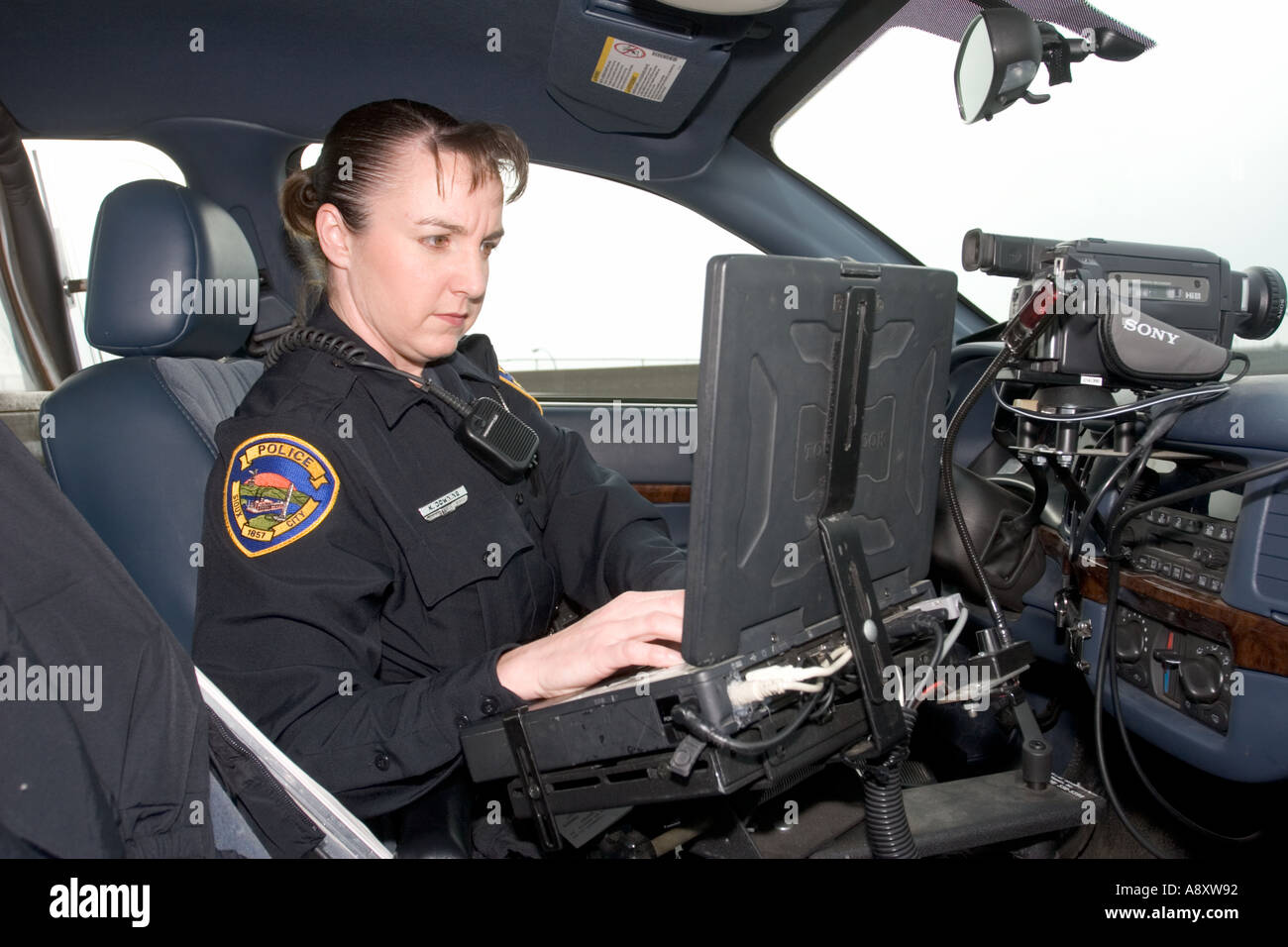 Female police officer using laptop in her police cruiser to check a drivers license. Sioux City, Police Department, Iowa, USA. Stock Photo