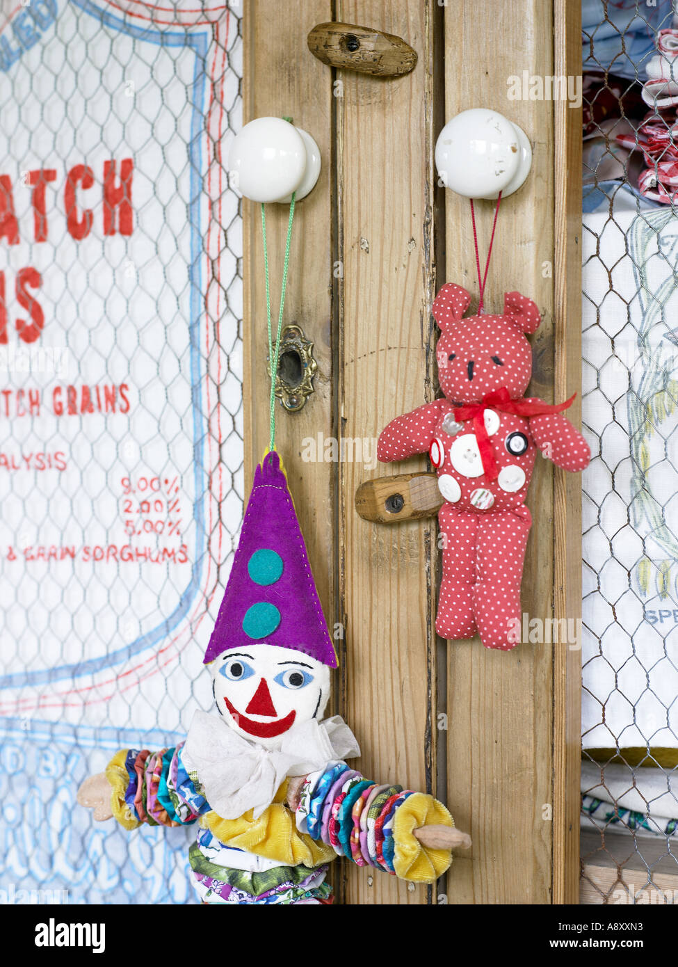 old rag clown and teddy bear with buttons hanging on a cupboard with chicken wire doors Stock Photo