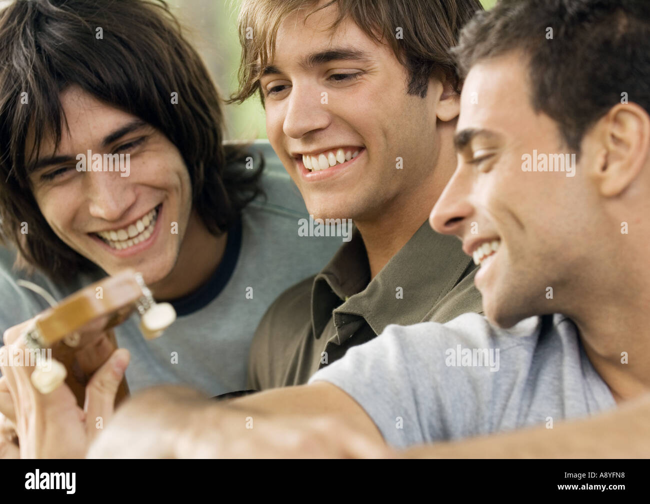 Three young male friends, looking at guitar Stock Photo
