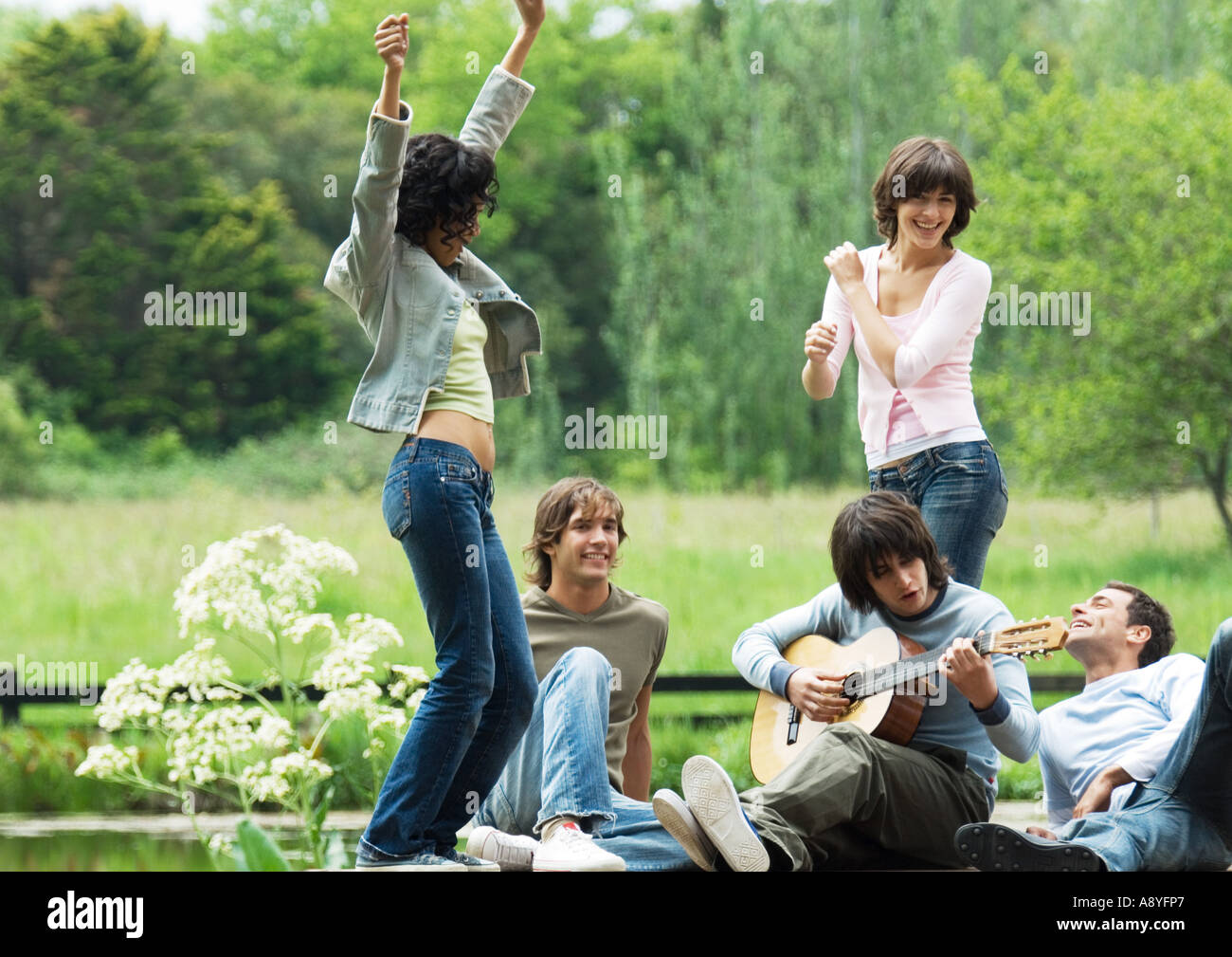 Group of friends outdoors, young women dancing while young man plays guitar Stock Photo