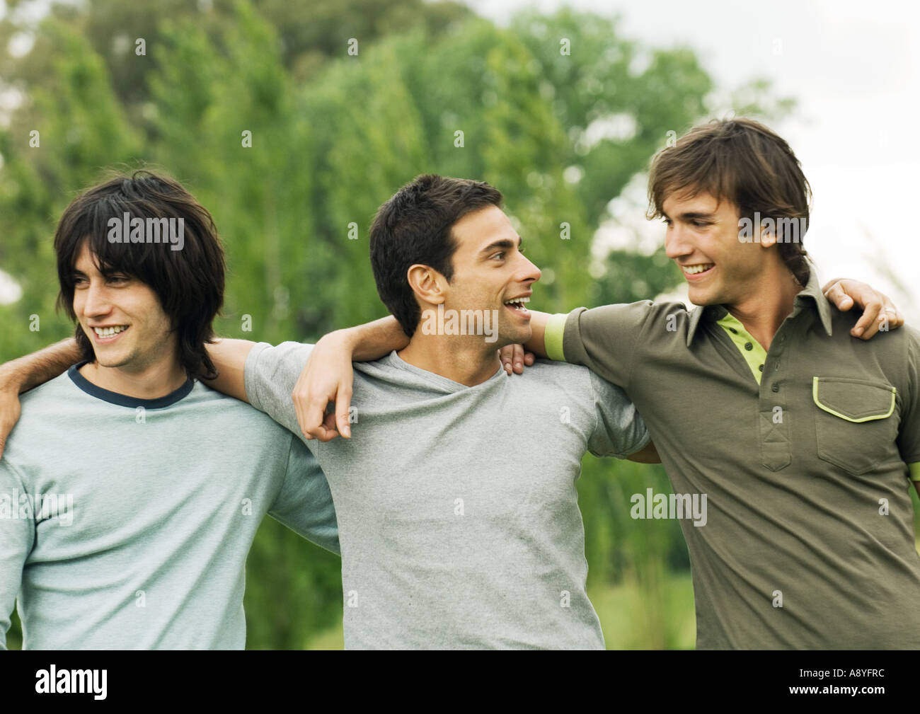 Three young male friends with arms around each other's shoulders Stock