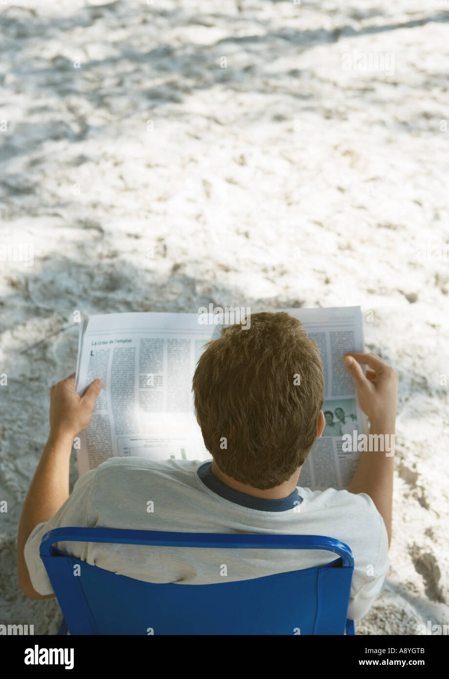 Man sitting in beach chair reading newspaper, rear view Stock Photo