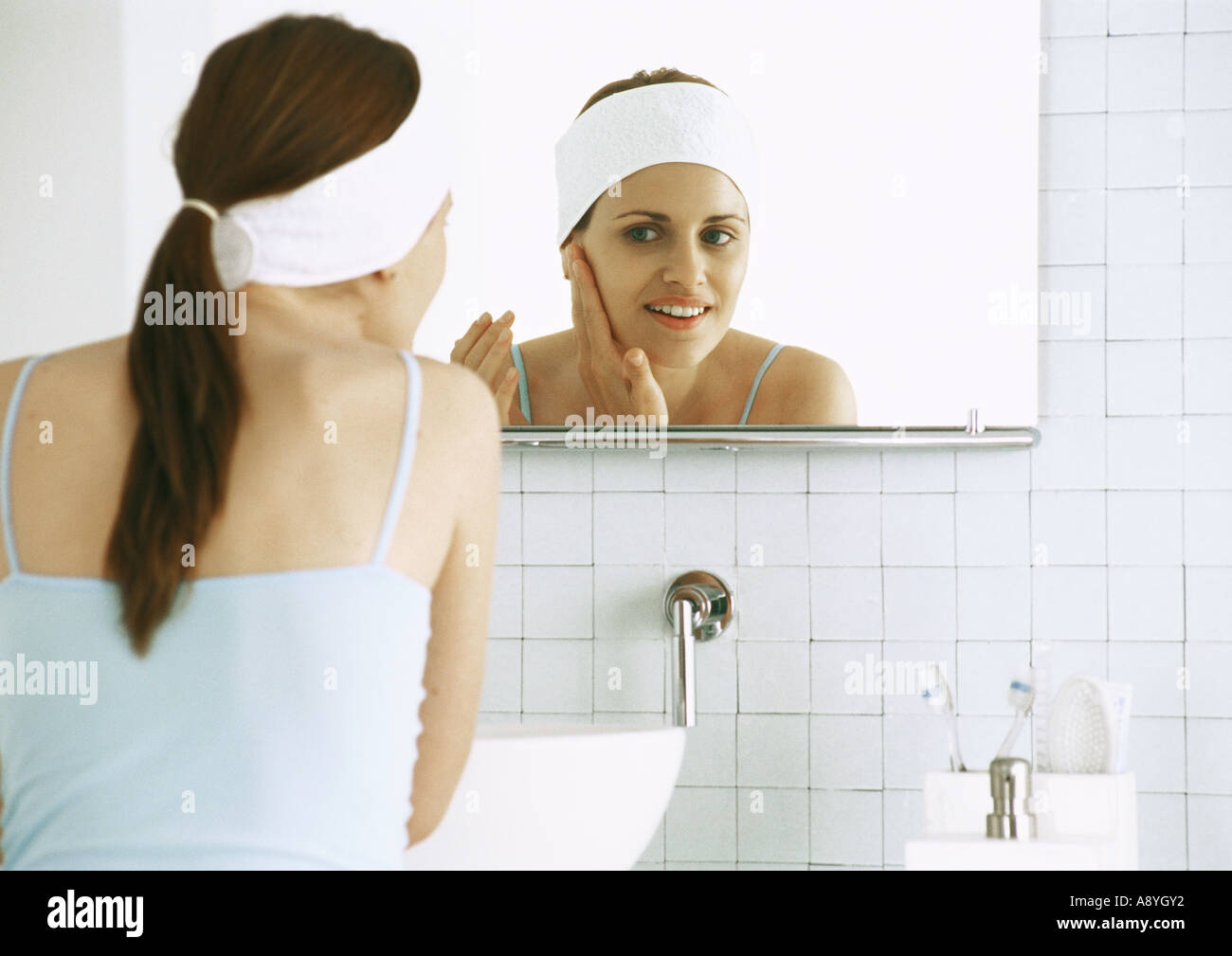 Woman looking in bathroom mirror, rubbing face Stock Photo