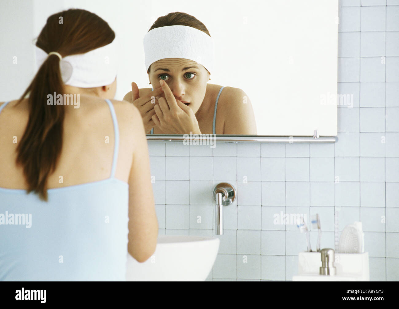 Woman standing in front of bathroom mirror, inserting contact lens Stock Photo