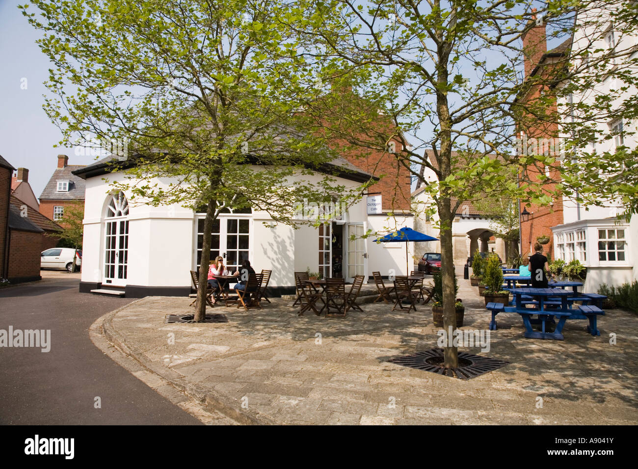 Square with trees and waitress serving outside table customer / customers tables at the Octagon cafe Poundbury Dorchester Dorset UK Stock Photo