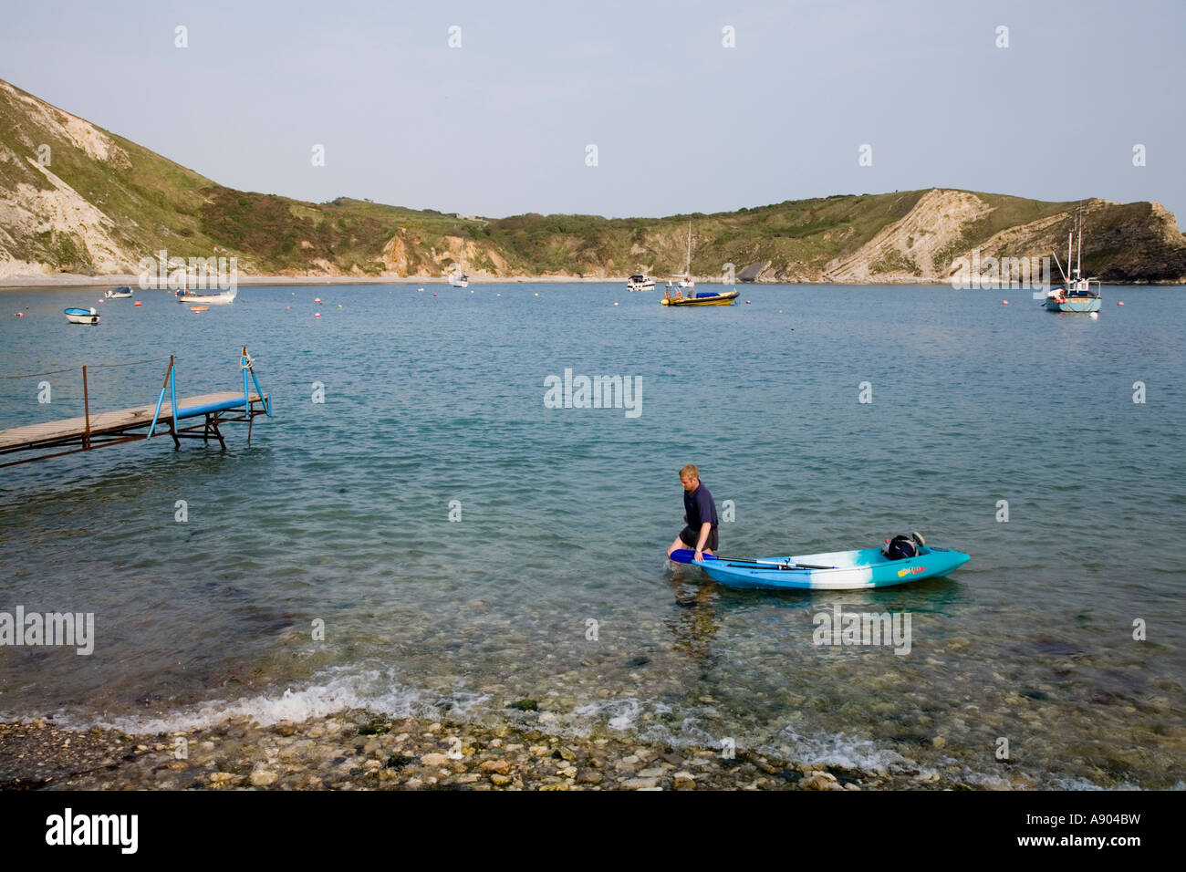 Tourist towing a canoe kayak to the jetty in Lulworth Cove Dorset UK Stock Photo