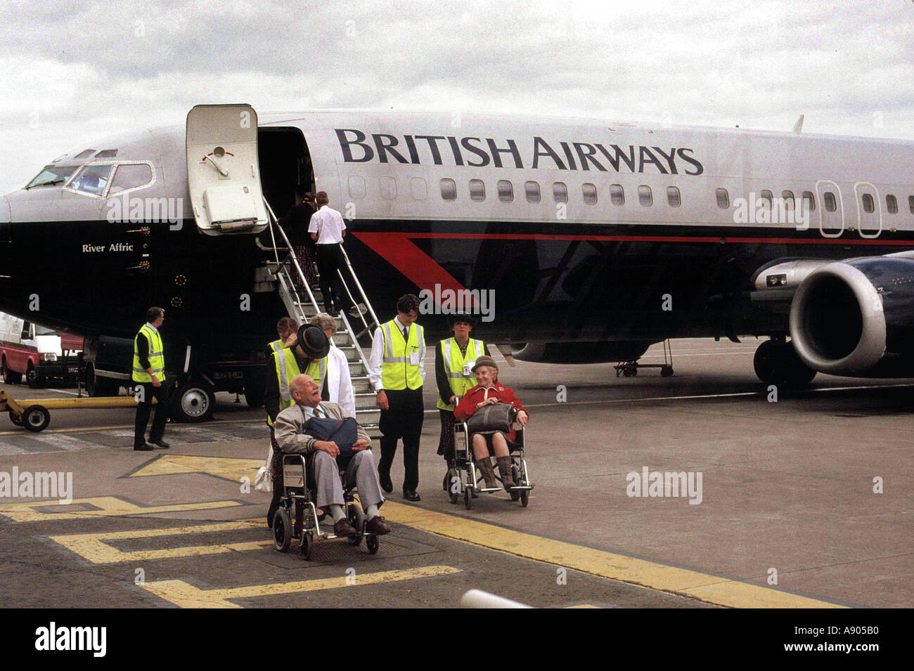 air stewardess pushing old couple in wheelchairs on airport tarmack