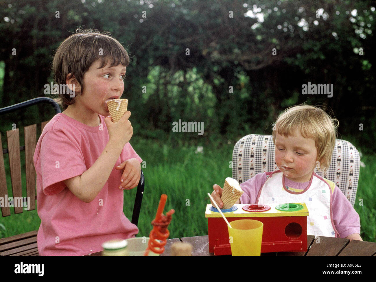 two young children eating ice cream and playing with toys Stock Photo