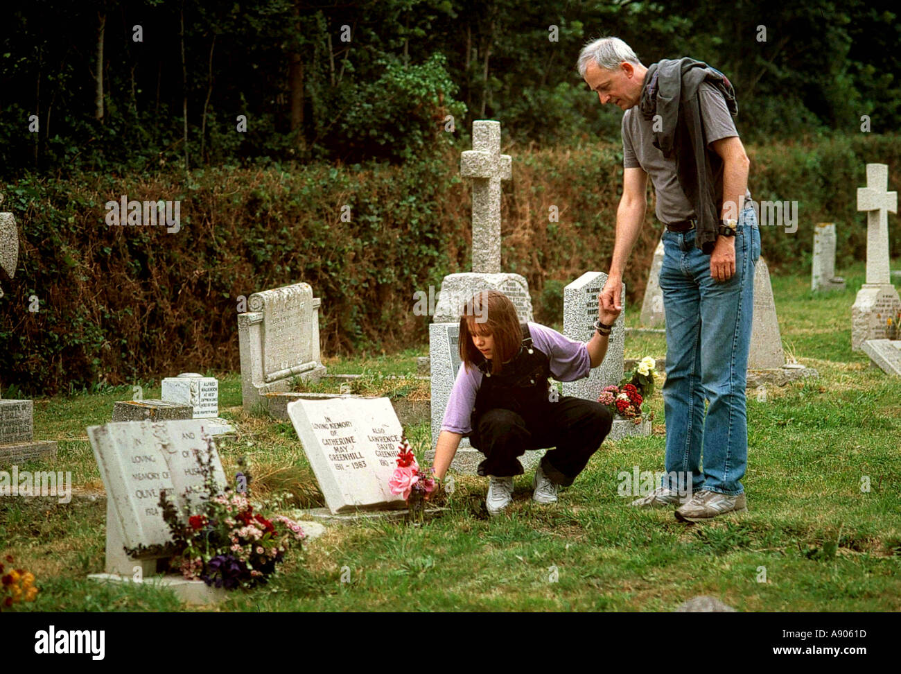 Father and daughter in a churchyard placing flowers on a grave Stock