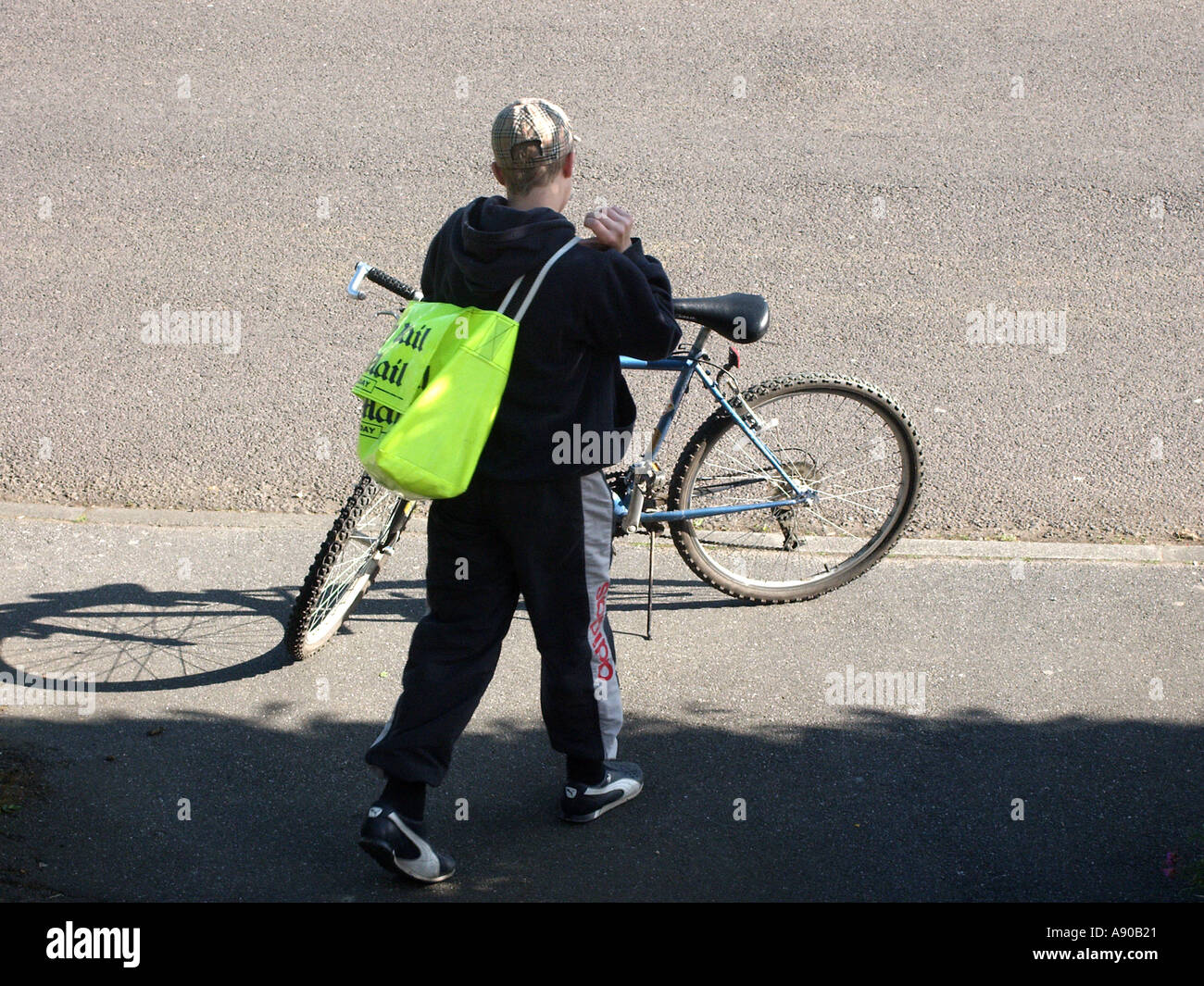 Newspaper delivery paper boy back view returning to bike to continue round after delivering to front door of residential property Essex England UK Stock Photo