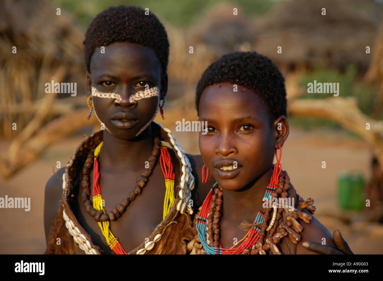Two colourful decorated girls of the Hamar people in front of a straw hut village in the savannah Turmi Ethiopia Stock Photo