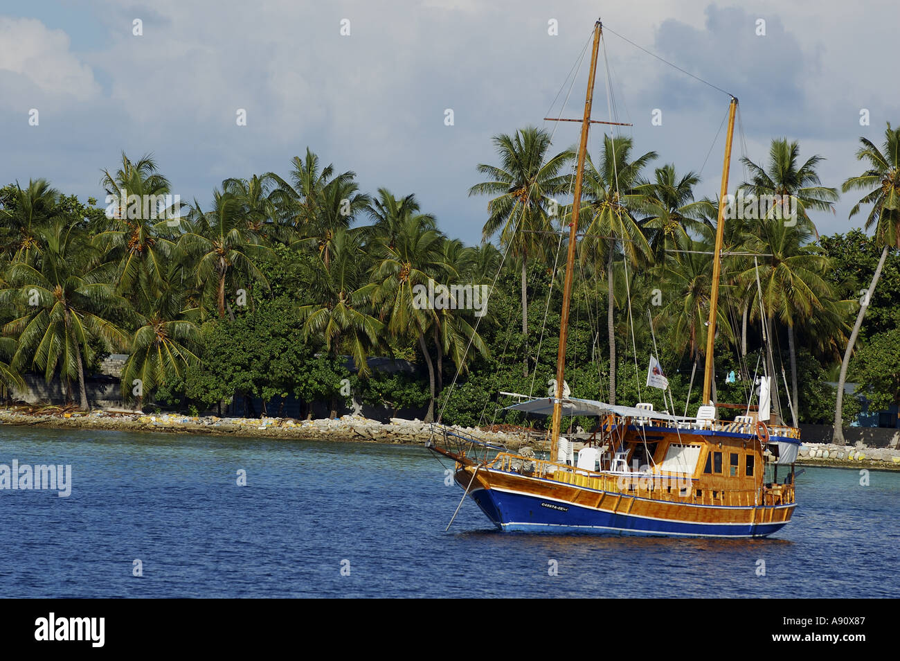 Wooden sailboat moored in the sea near a palm covered beach, Maldives. Stock Photo
