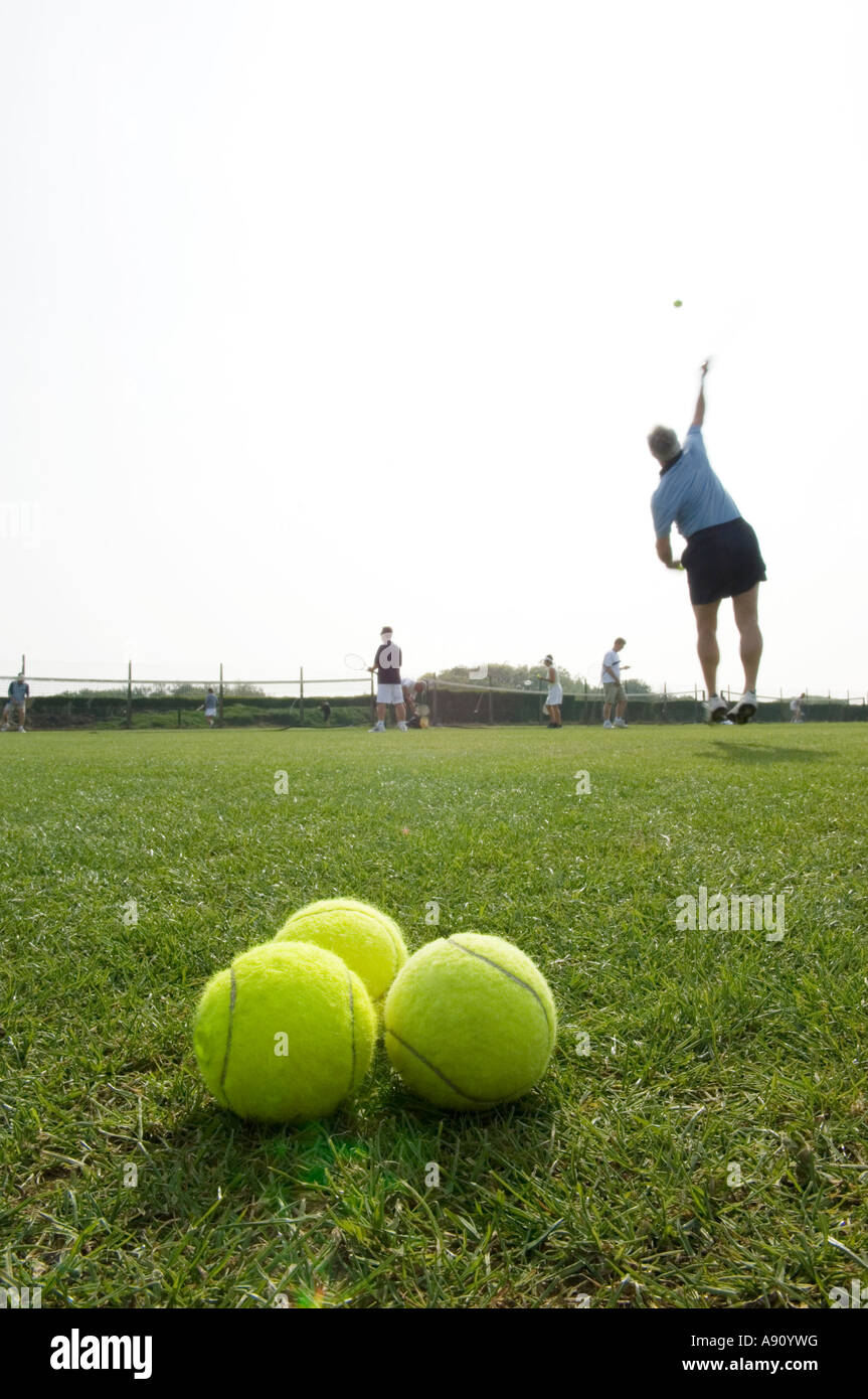 Three tennis balls with out of focus player serving in the background Stock Photo