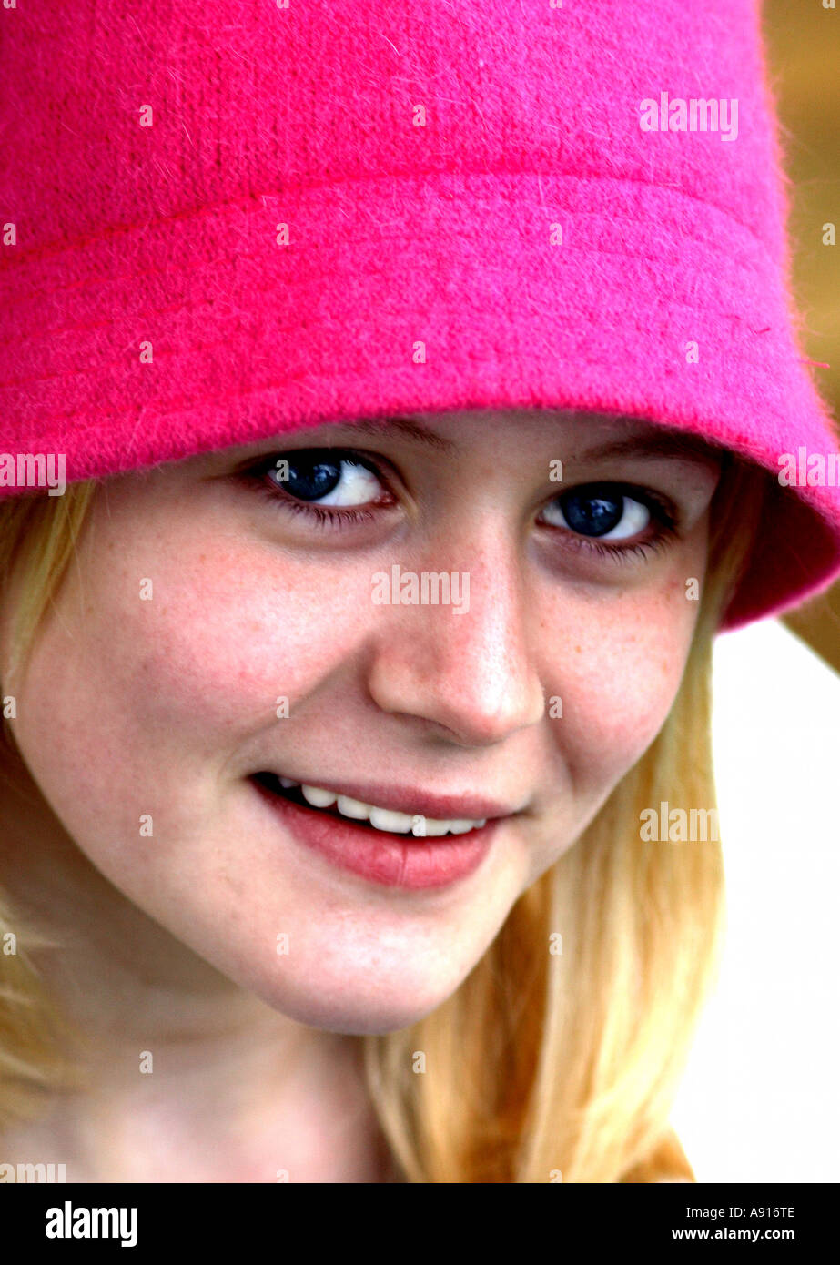 Vertical close up portrait of pretty young blonde woman smiling at camera,  wearing bright colour pink cloche hat Stock Photo