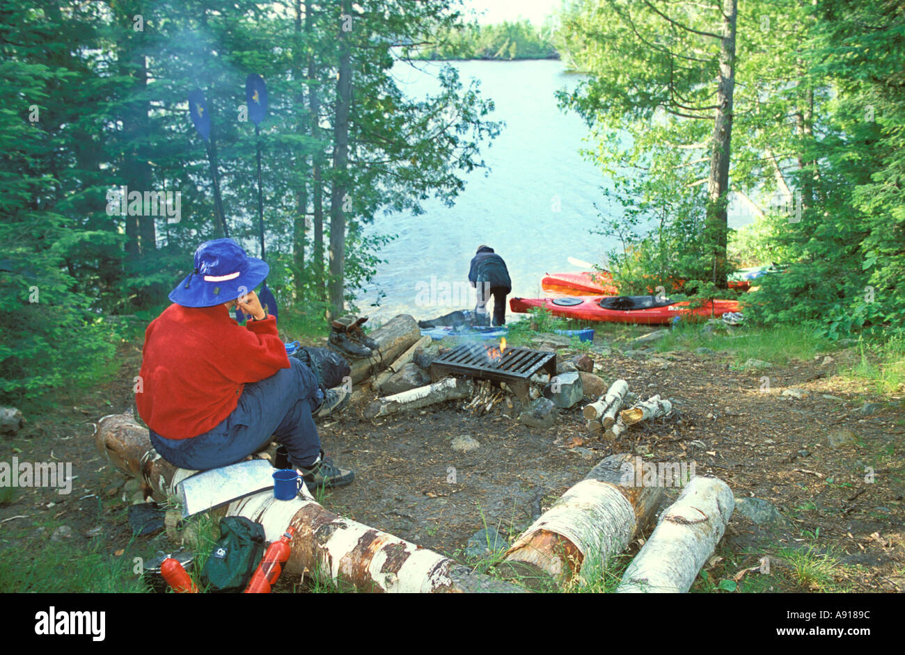 A camper sitting by a fire at a camp site in the Boundary Waters Canoe Area Wilderness Minnesota Stock Photo
