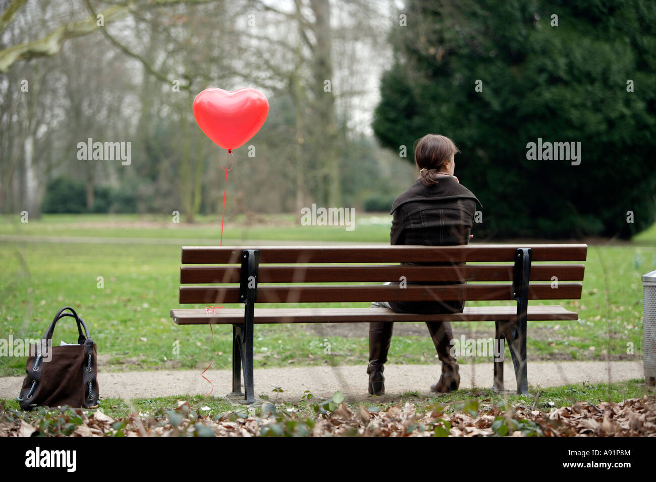 A young woman sits alone on a park bench Stock Photo