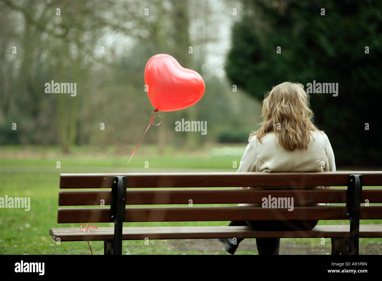 A young woman sits alone on a park bench Stock Photo