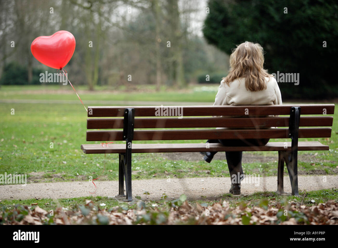 A young woman sits alone on a park bench Stock Photo
