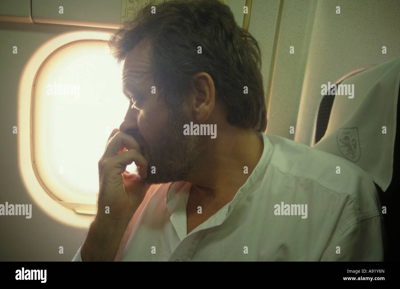 man on plane looking anxiously out of window Stock Photo