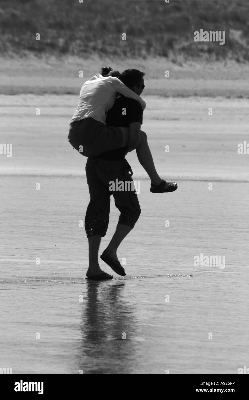 Young man carrying young woman on piggy back to keep her feet dry, Enniscrone / Inishcrone, County Sligo, Ireland Stock Photo