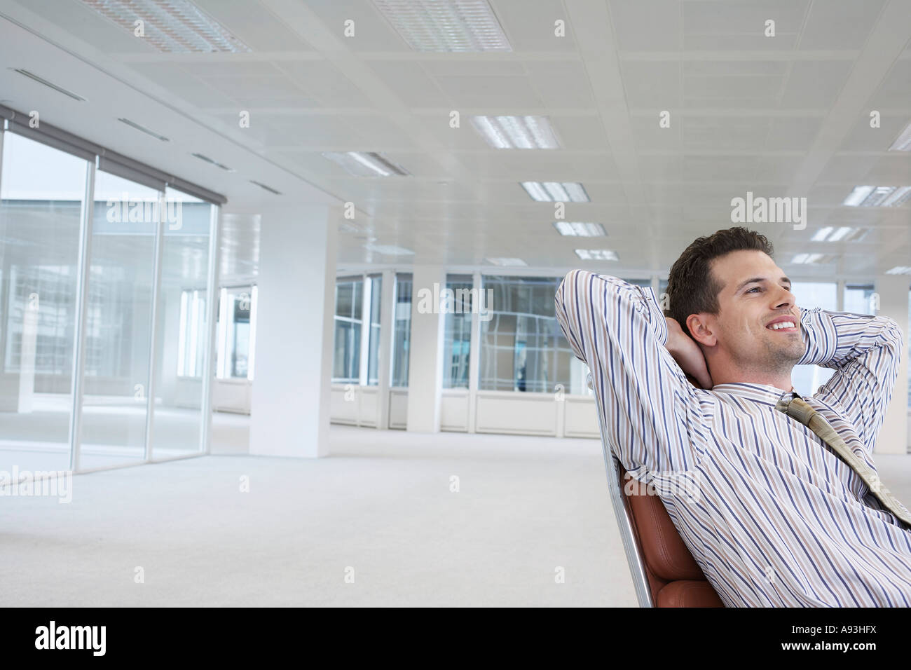 Office worker leaning back in swivel chair, hands behind head, in empty