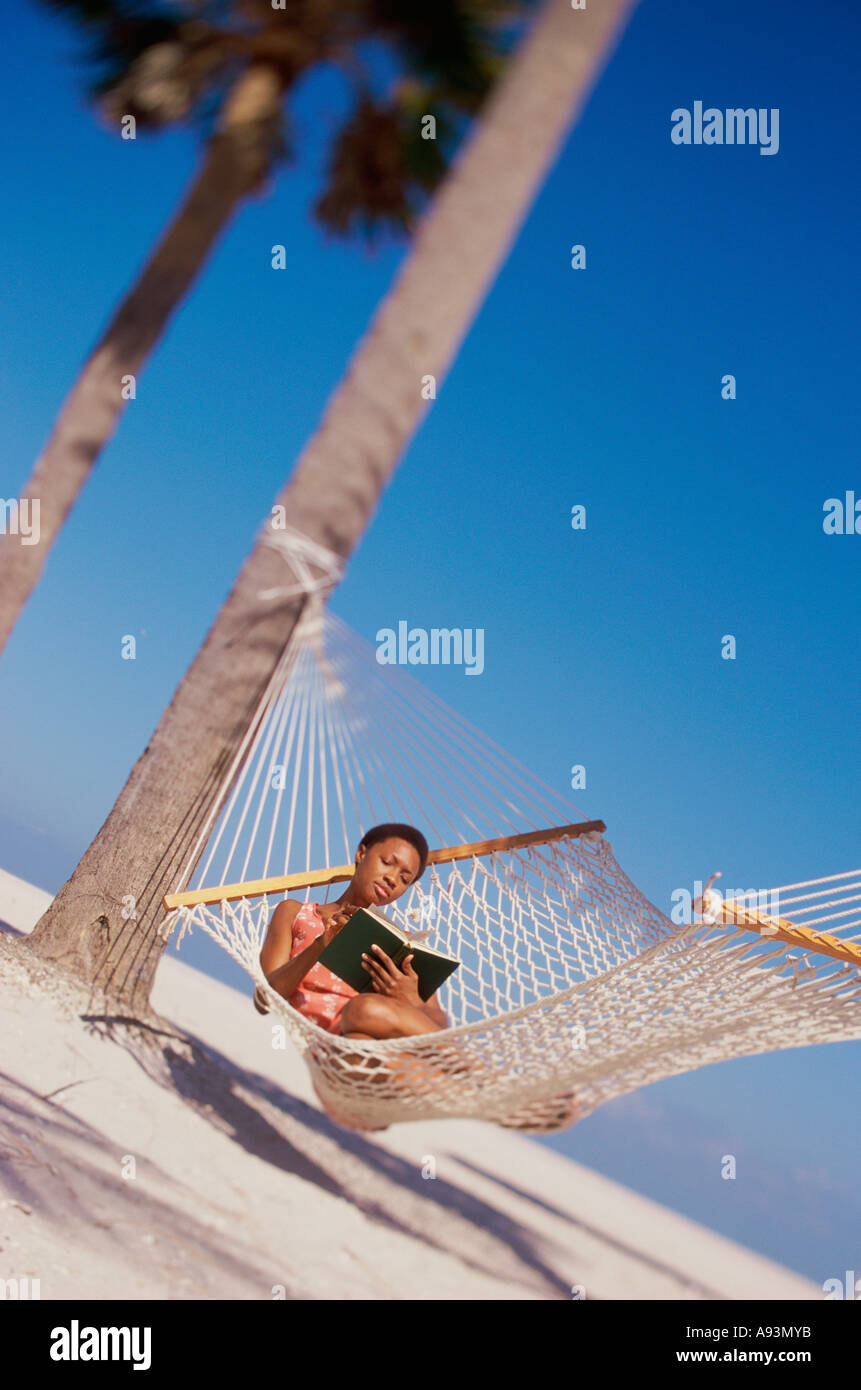 Young woman lying down in a hammock and reading a book Stock Photo