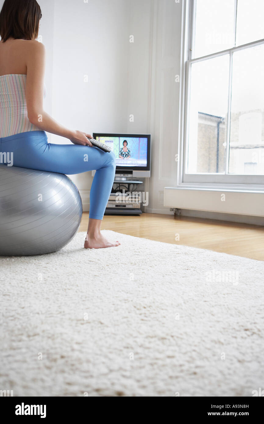 Woman sitting on fitness ball, watching television, back view Stock Photo