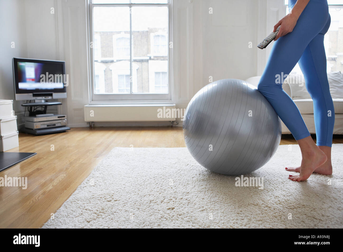 Woman standing at fitness ball, watching television, low section Stock Photo