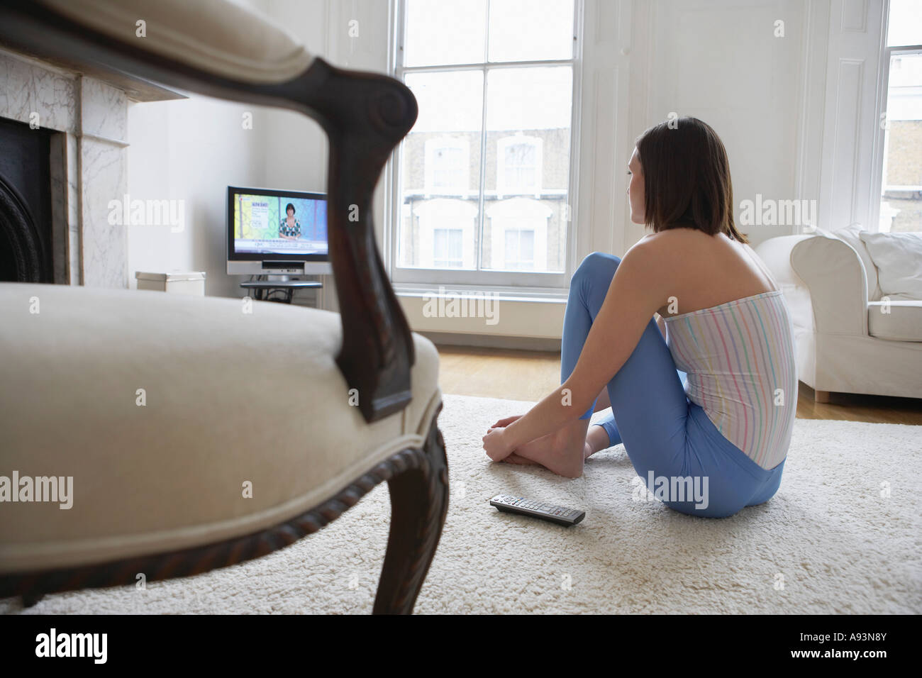 Woman sitting on floor, watching television, back view Stock Photo
