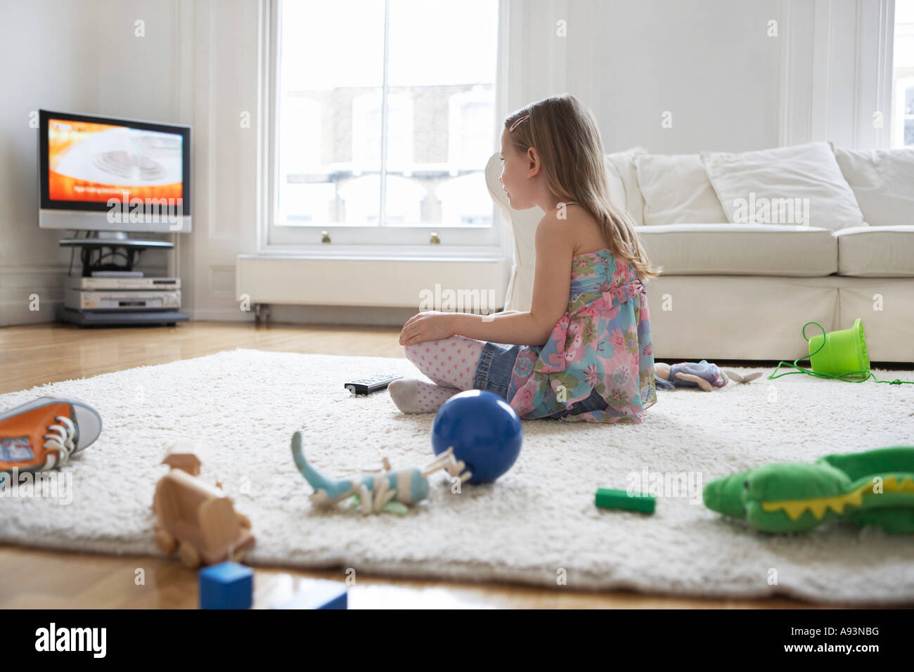 Girl (5-6) sitting on floor surrounded with toys, watching television Stock Photo