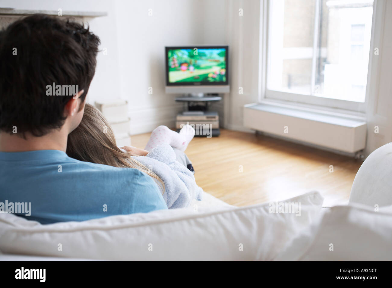 Father and daughter (5-6) watching cartoons in television, back view Stock Photo