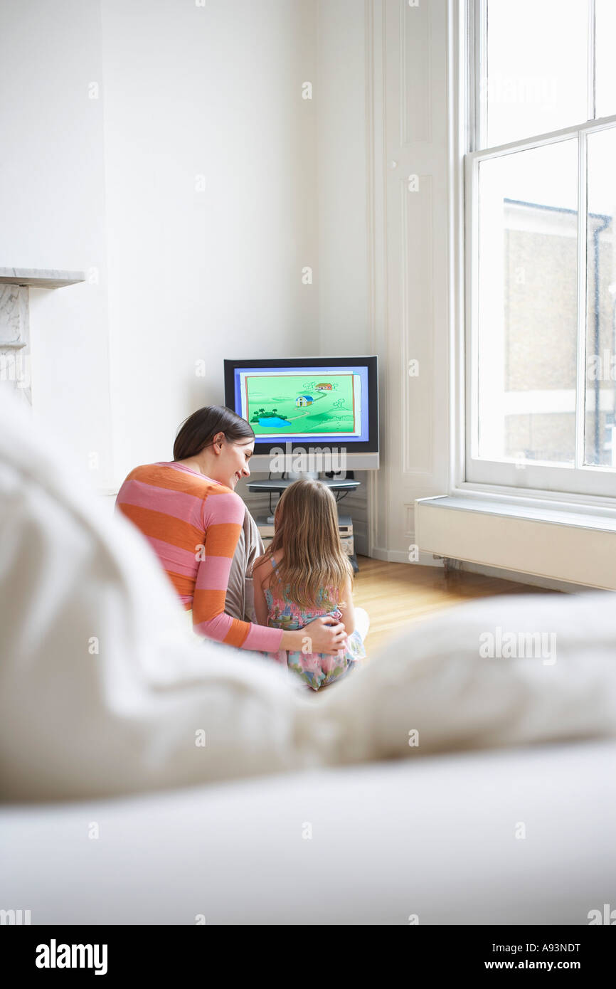Mother and daughter (5-6) watching cartoons in television, back view Stock Photo
