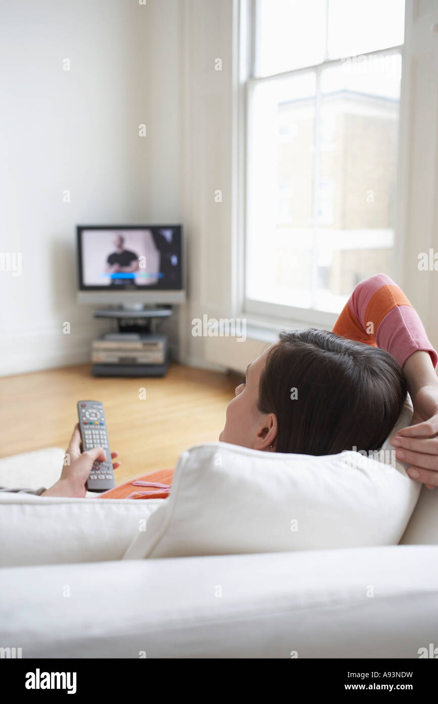 Woman lying on sofa, watching television Stock Photo