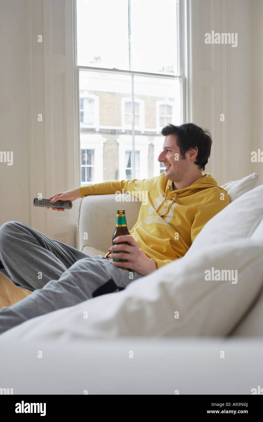 Man sitting on sofa, watching television and holding beer bottle Stock Photo