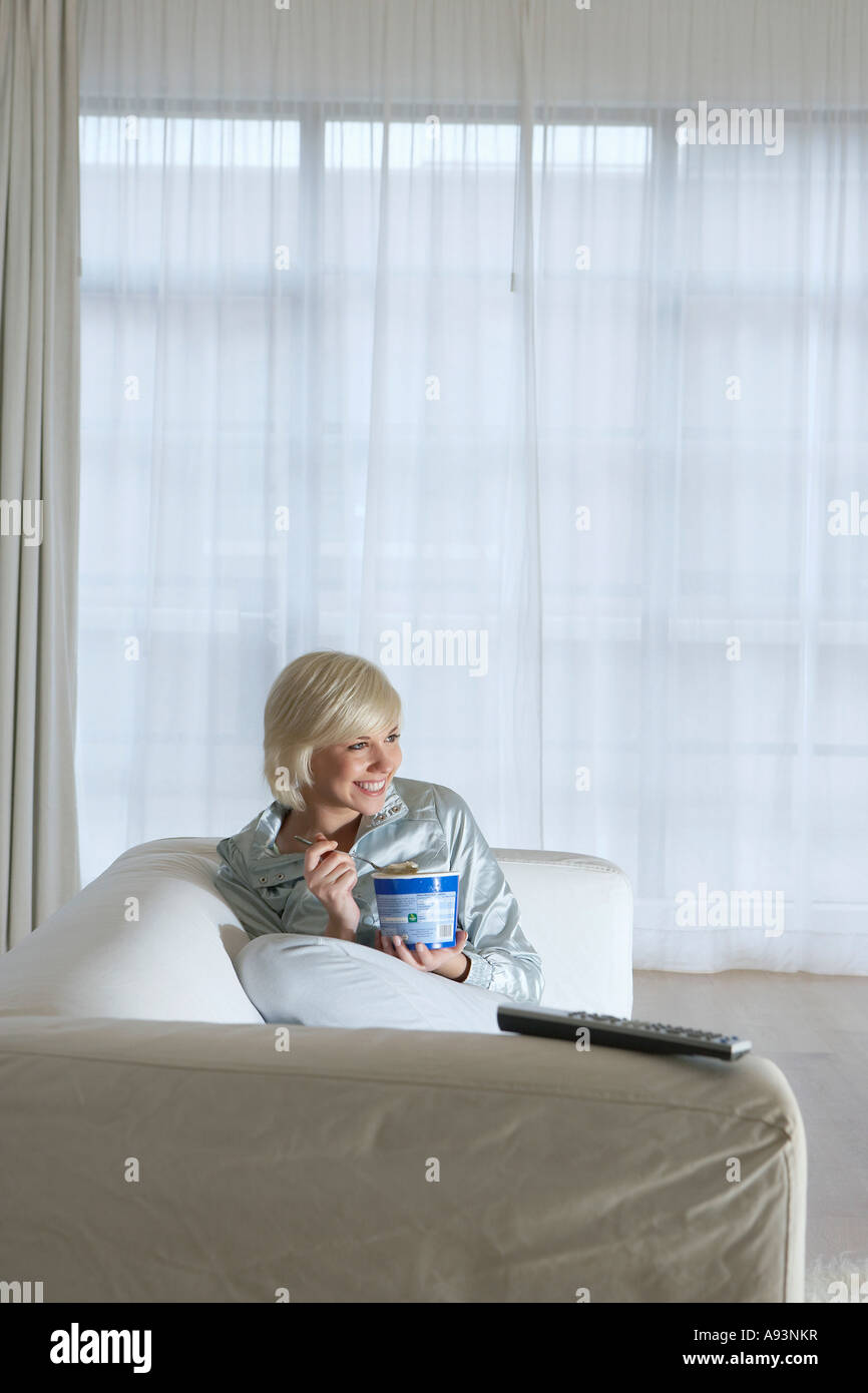 Woman sitting on sofa, watching television and eating ice cream Stock Photo