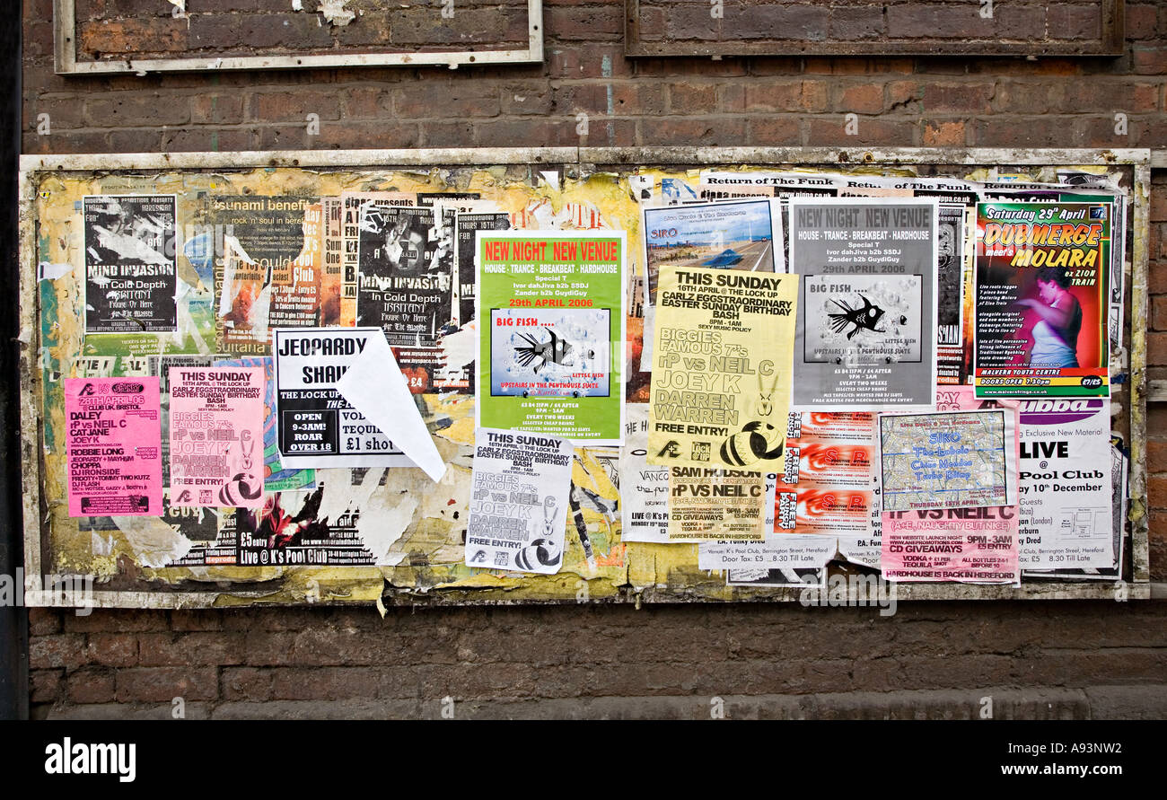 Torn and tatty posters pasted to a faded board in a back street Hereford England UK Stock Photo