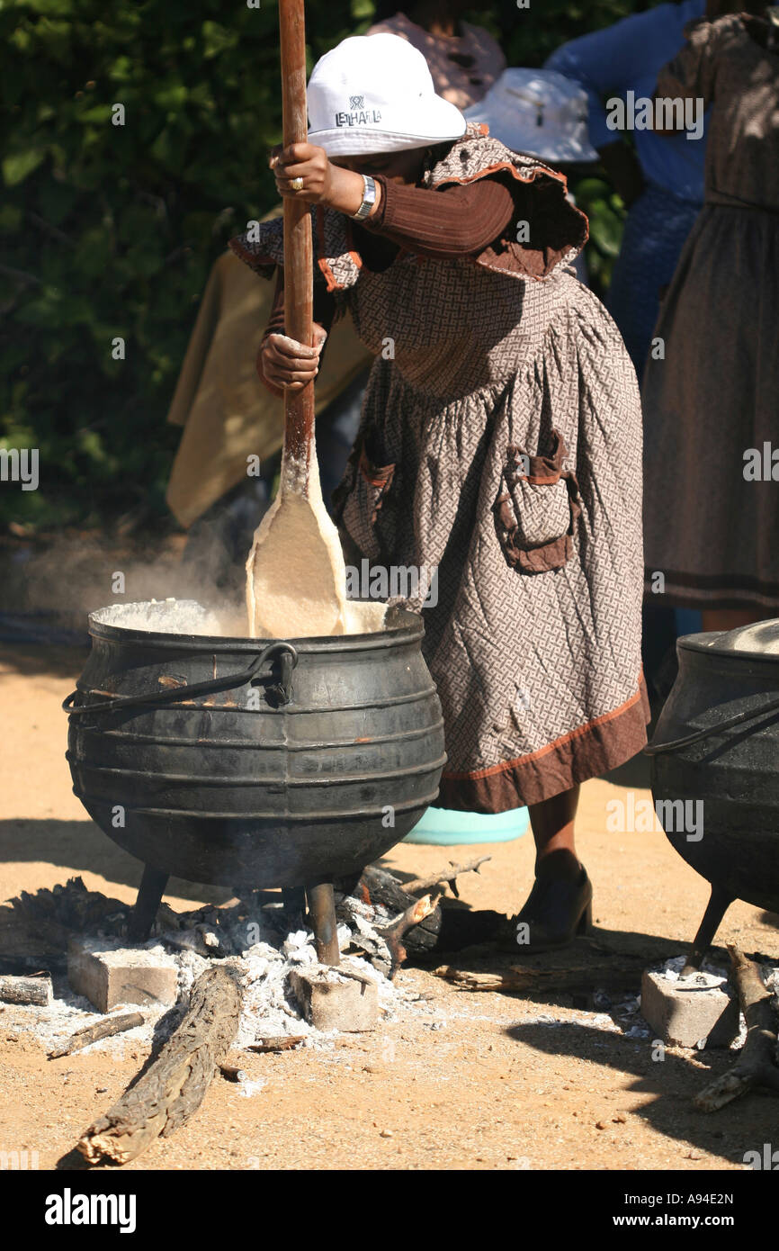 Motswana woman preparing traditional porridge in a three legged iron