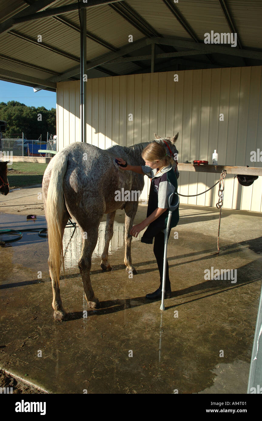 Young woman with one leg  washing down her horse after riding for disabled competition Stock Photo
